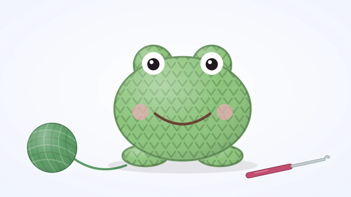 Round green crocheted frog with two eye bumps on top of its head, a wide smile, pink cheeks and small feet